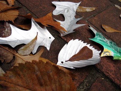 Leaves made out of old aluminum cans lay on the ground next to real autumn leaves.