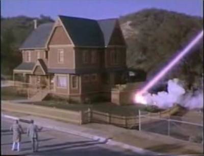 Two people look at a house as a large laser beam blows it up.