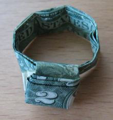A two dollar bill on a table folded up to resemble a bracelet.