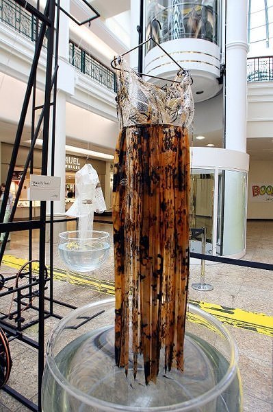 A dress made of tattered brown fabric hanging above a tub of water.