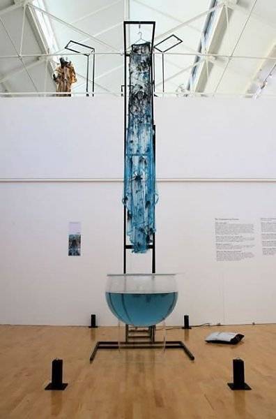 A dress specially engineered to melt in water is hanging above a glass tub.