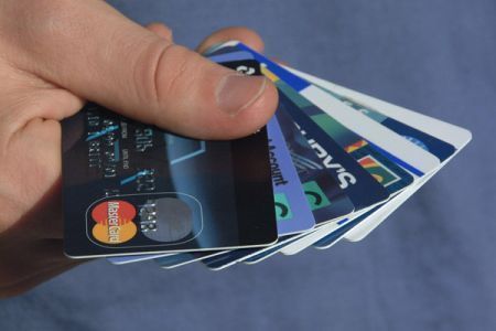 A person holding 8 credit cards fanned out in their hand, against a blue background.