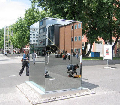 A toilet cubicle with mirrored walls sits in a very public space.