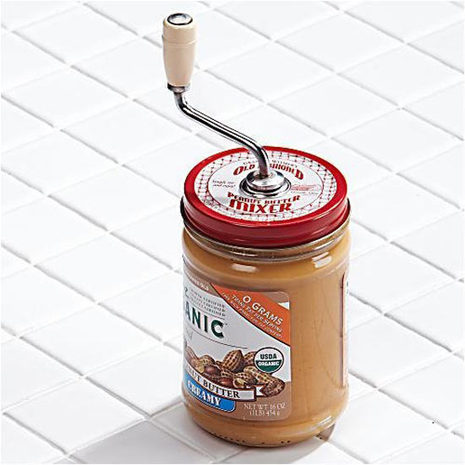 A mixing device is inside a jar of natural peanut butter, which needs to be stirred due to separation.