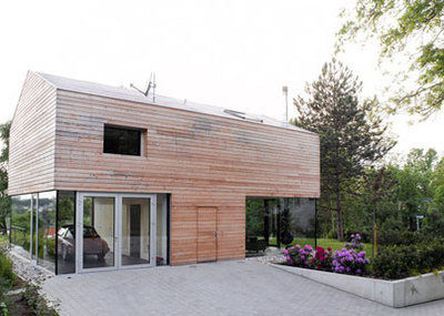 A garage made of hardwood and glass walls sits in a green and leafy yard.