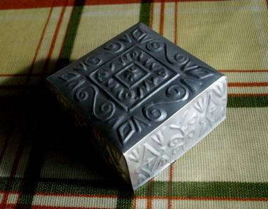 A decorated grey box sits on a plaid blanket.