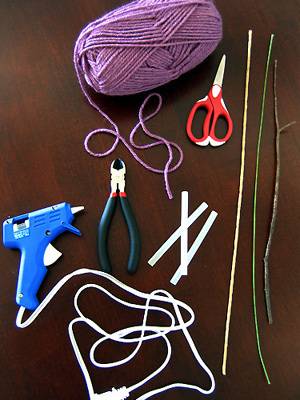 A hot glue gun, pliers, scissors, and various types of yarn lay on a table.