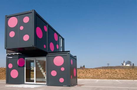 Shipping containers made into a two story house that is painted black with pink polka dots.