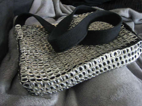 A silver, textured purse has a large black strap.