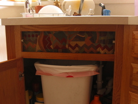 A white trash can with a white trash liner in it sitting under a kitchen sink.
