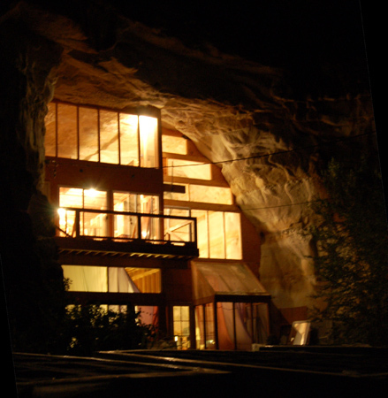 A cave house made of wood and glass is glowing in the dark.