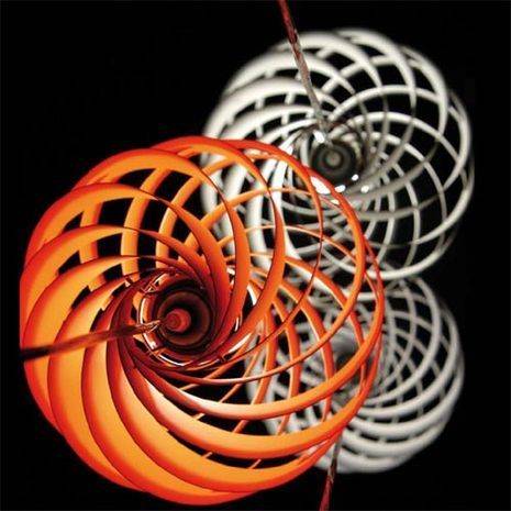 An orange curled up slinky next to a white slinky with a black background.