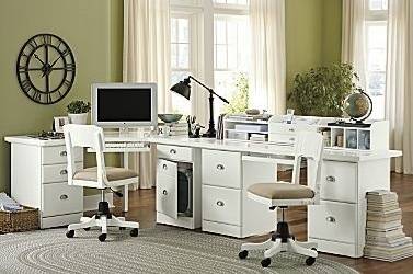 Computer monitor on top of L-shaped white desk next to chair and stool.