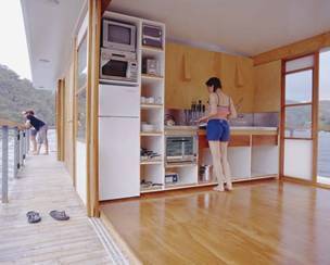 A woman stands in the kitchen area of a houseboat where the entire room is open to the outdoors.