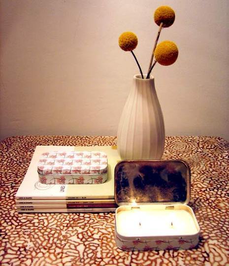 Three round brown bulbs sticking out of a tan vase next to an open tin and some books laying down with anothe rtin on them.