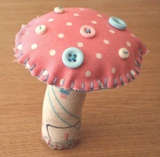 A fabric toadstool with a pink polka dot head dotted with pastel colored buttons.