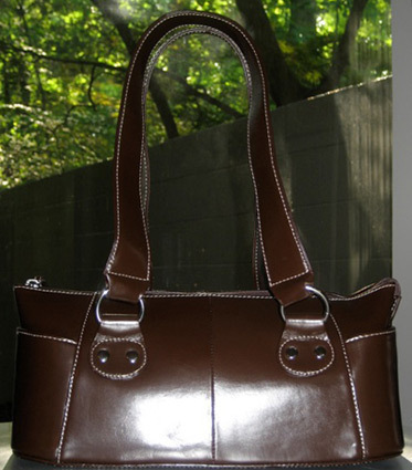 A shiny, dark brown leather handbag sits on a table outdoors.