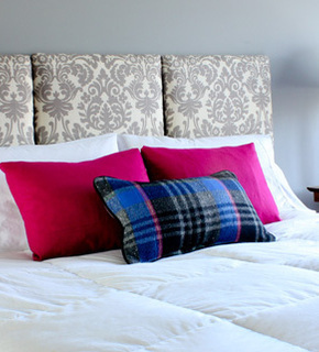 A decorative headboard on a bed with two red pillows and a blue plaid pillow.