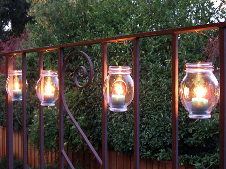 Glass jar lanterns with lit candles inside hang from a gate.