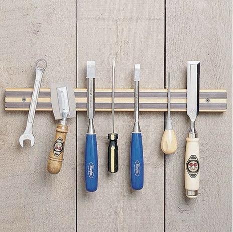 Various tools hanging from a magnetic strip screwed to a pale wooden wall.