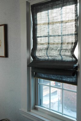 An interior view of window with a sheer shade raised halfway up.