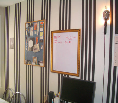 Several paintings on a blue striped wall over a blank computer monitor.