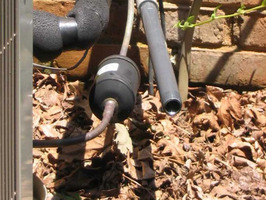 A metal pipe and other tubes jut out from a brick structure near the ground.