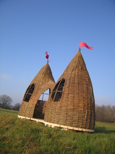A large wooden tee pee in the grass.
