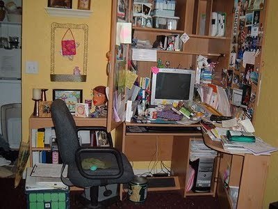 An office chair sits in front of an extremely cluttered computer desk.