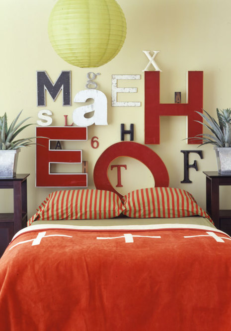 A bed with and orange comforter and letters on the wall behind it.