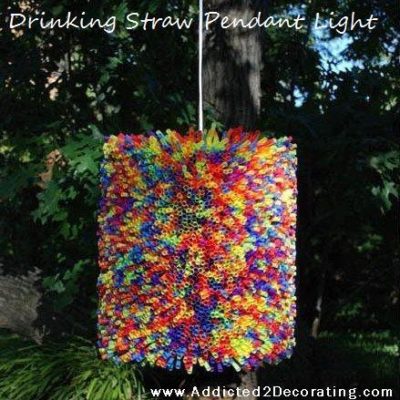 Multicolored pendant light made with drinking straws hanging to a tree in the garden.