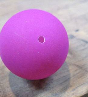 A hole in the top of a fuchsia ball on a marble countertop.