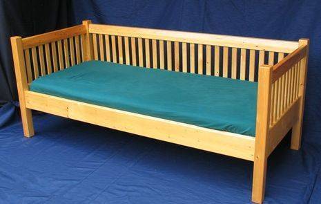 A wooden futon with slatted rails encases a thin mattress.