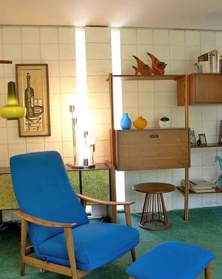 A royal blue chair and Ottomans in mid century style sit in front of mid-century storage cabinet and bookshelves.