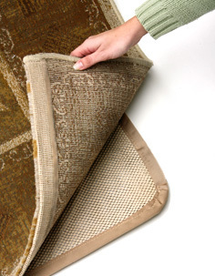 A woman partially pulling up a rug to reveal the skid cover underneath.