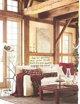 A cozy red throw is over the arm of a beige couch and a mountain cabin style home.