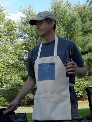 Man with spectacles holding drink bottle with hand wear apron stands in the garden.