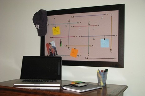 A memo board sitting over a computer desk with a New York Yankees hat on it.