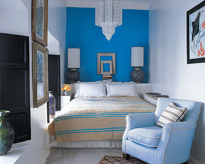 A blue chair is at the foot of a bed in a room with blue and white walls.