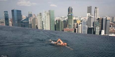 A person is swimming in an infinity pool next to a downtown cityscape.