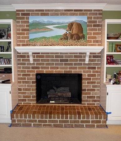 An empty fireplace with a landscape painting on top.