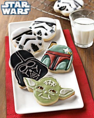 Decorated star wars cookies, Darth Vader, Yoda, and Stormtroopers on a white plate over a red napking and next to a glass of milk.