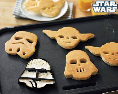 Star wars cookies, darth vader, yoda and a stormtrooper are on a black cookie sheet.