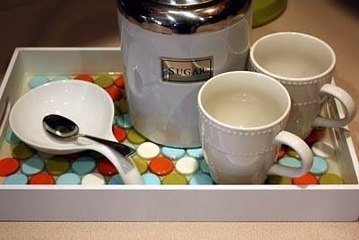 A kitchen tray holding a couple mugs and a tablespoon that is made out of bottle caps on the bottom.
