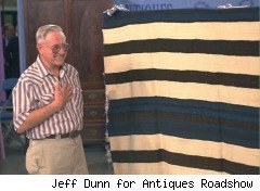 An older man shows off a blanket of some sort for Antiques Roadshow.