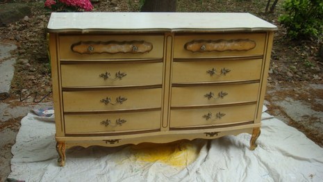 A tan dresser with eight drawers on a white cloth on pavement.