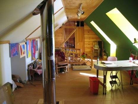 An attic workroom, with a green wall, skylights, a table and a pink chair.