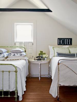 Attic with wood floors furnished with two twin sized beds with white sheets on them.