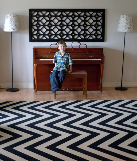 A young boy sitting on a piano bench on a black and white chevron floor.