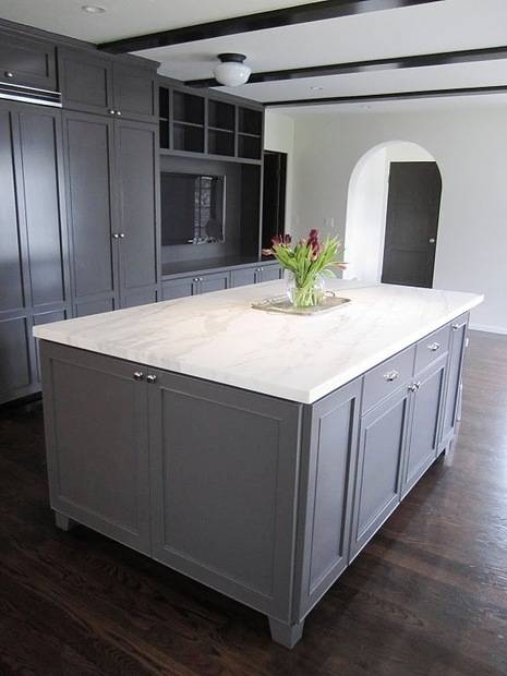 A white kitchen has a flower on the island.